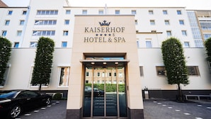 La entrada al Hotel & Spa Kaiserhof, con fachada moderna, grandes puertas de cristal y un área de estacionamiento visible al fondo.