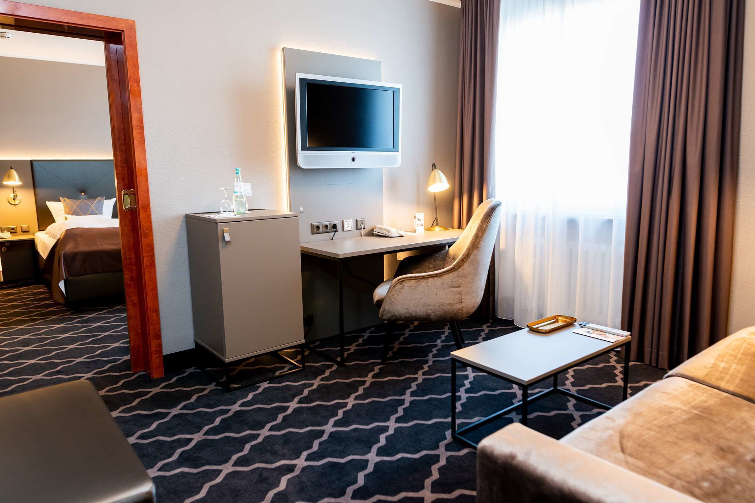 Ein Hotelzimmer mit Bett, Schreibtisch mit Computer, Stuhl, einem kleinen Tisch und einem an der Wand befestigten Fernseher.