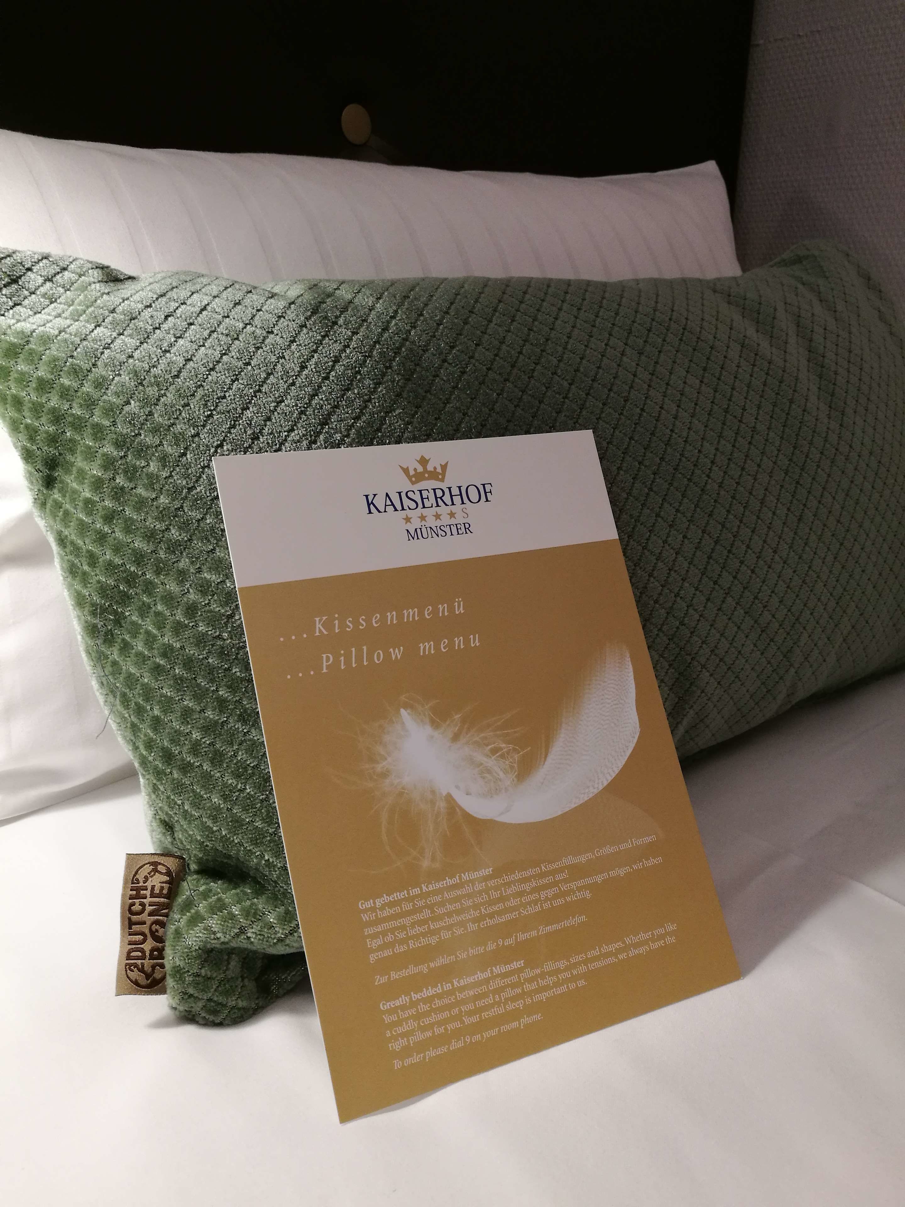 Un oreiller muni d’une étiquette indiquant qu’il provient de l’hôtel Kaiserhof Munster, et accompagné d’une carte proposant différents types d’oreillers.