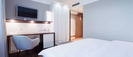 Una habitación de hotel moderna con una cama, un escritorio con una silla, un televisor y un armario.