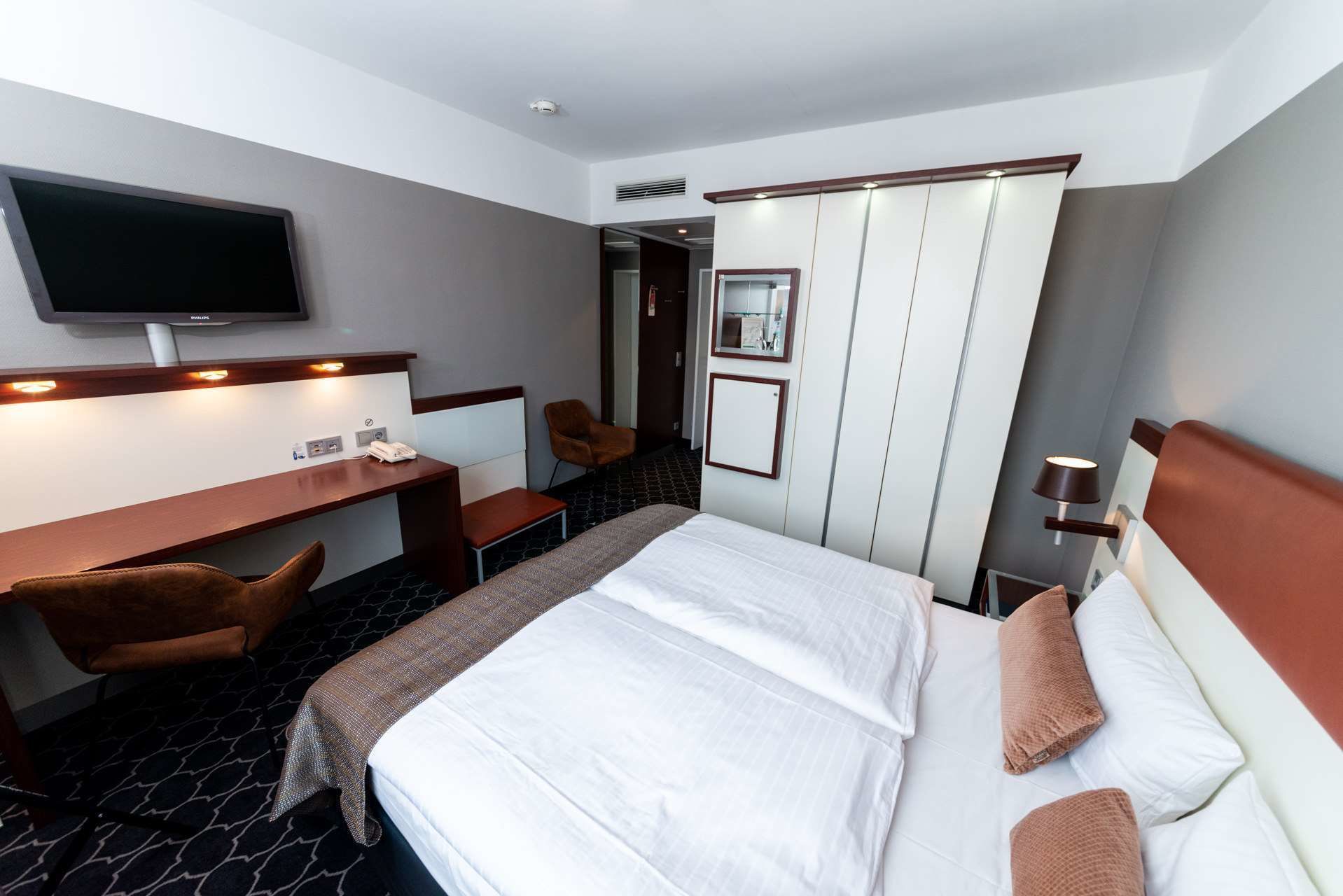 A hotel room with a bed, a desk, a chair, a television, and a wardrobe.