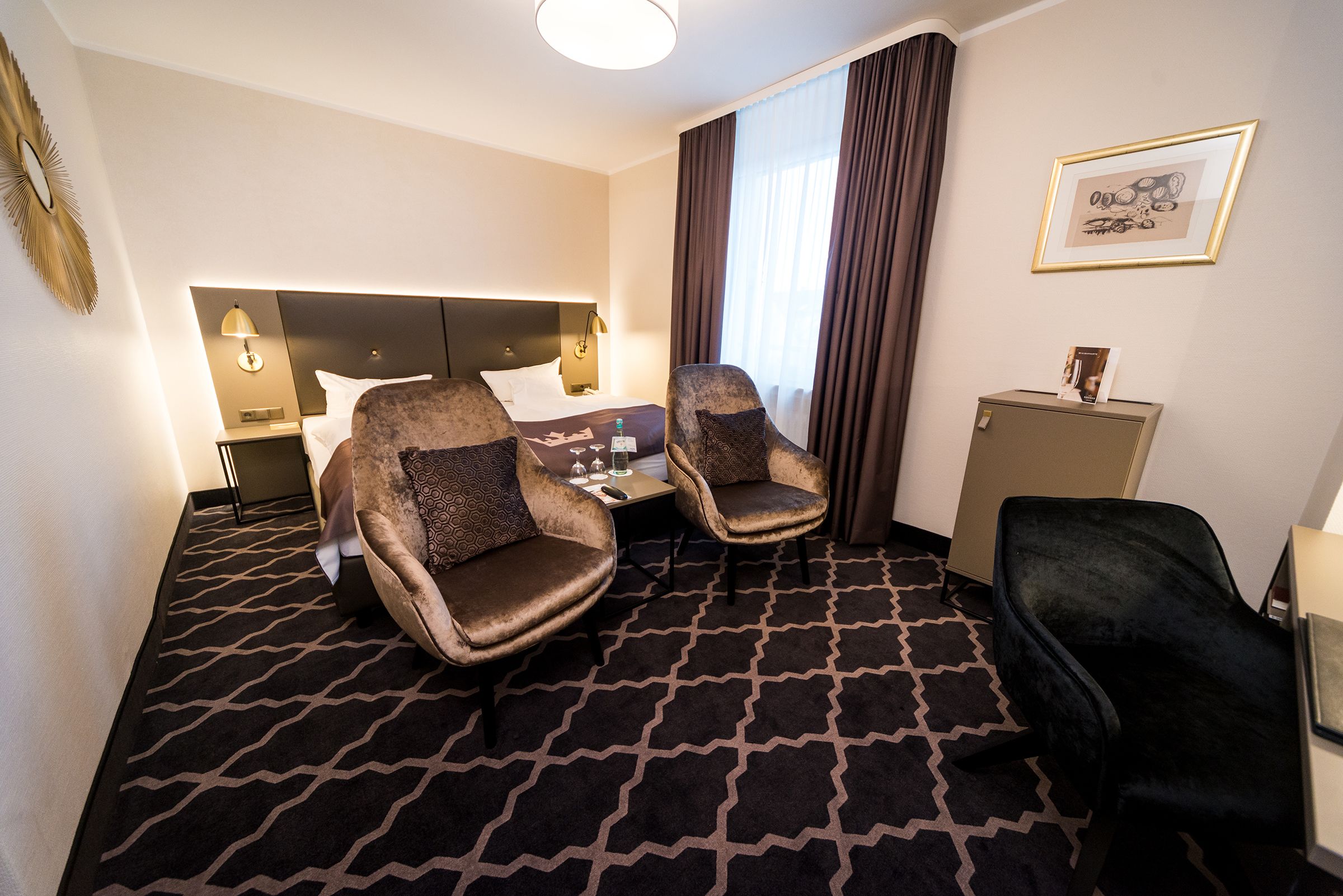 Habitación de hotel con cama, dos sillones, escritorio, mesita de noche y un pequeño armario.
