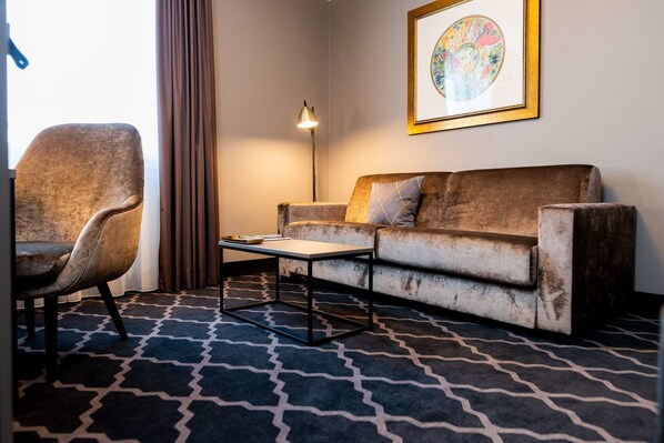 A room with a sofa, a chair, a coffee table, a floor lamp, and a framed picture on the wall.
