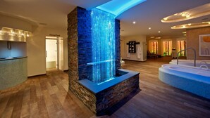 Zona de spa con cascada de piedra, un mostrador de recepción y una bañera grande.