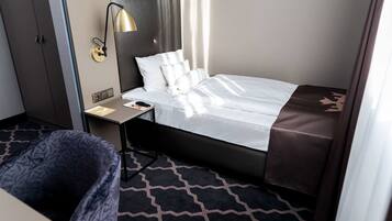 Une chambre d’hôtel avec un lit, une table de chevet, une lampe, une chaise et un tapis à motifs.