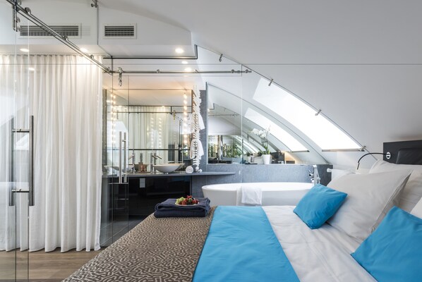 A modern hotel room with a large bed, a bathroom with a bathtub, and a skylight.