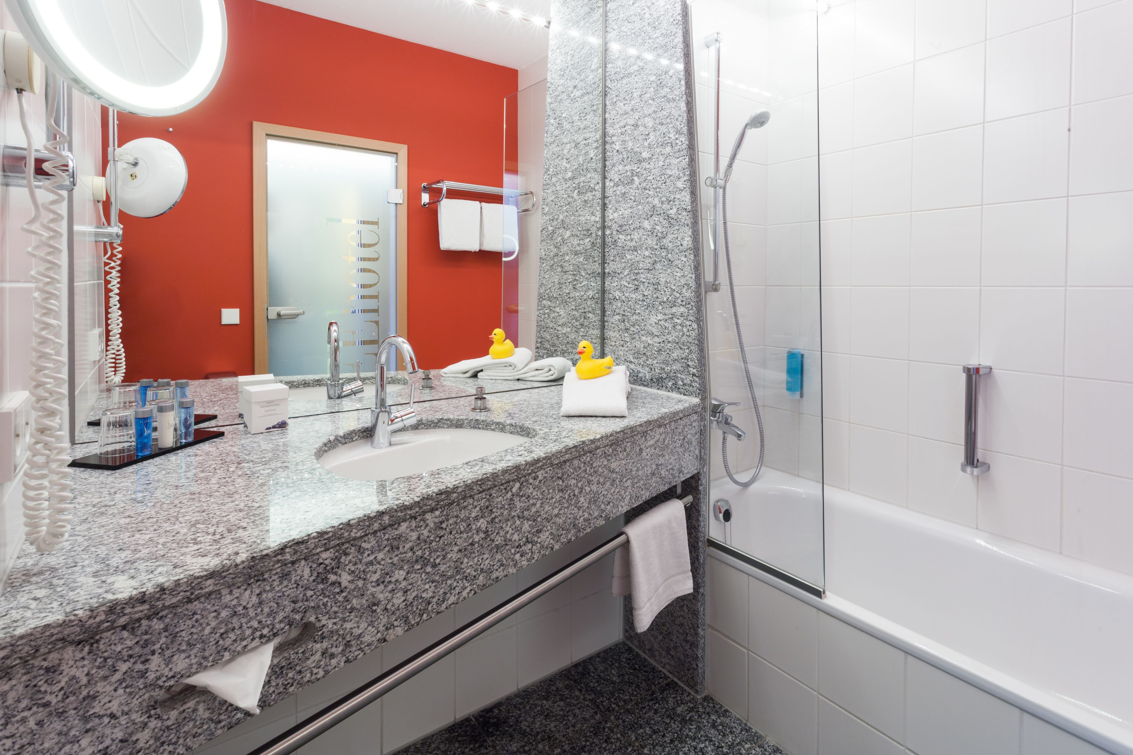 Une salle de bain moderne dotée d’un comptoir en granit, de deux vasques, d’un grand miroir, d’une douchette à main et d’une porte visible.