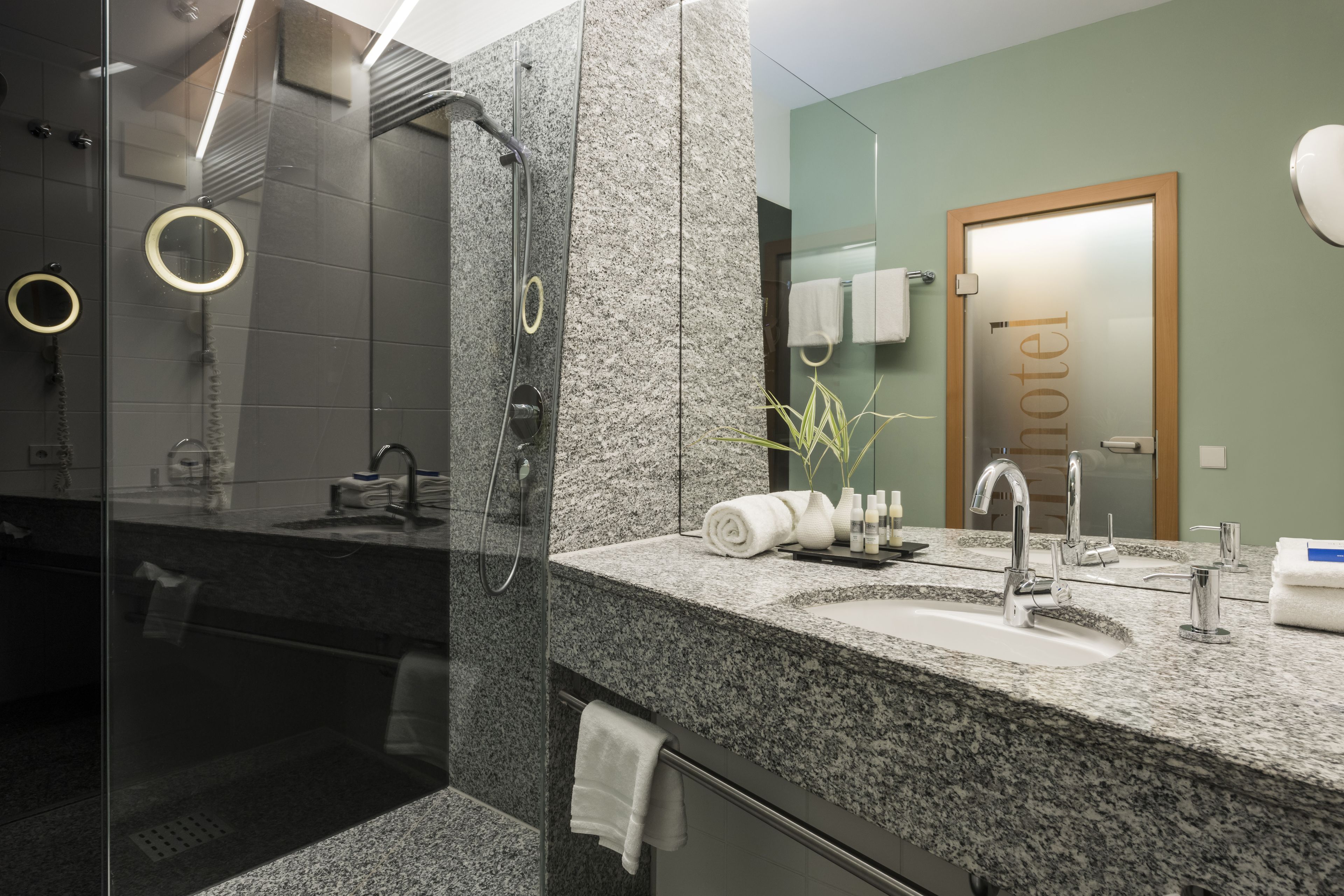 Een moderne badkamer met een granieten aanrechtblad, een douche met glazen wanden en een zichtbare handdoekhouder.