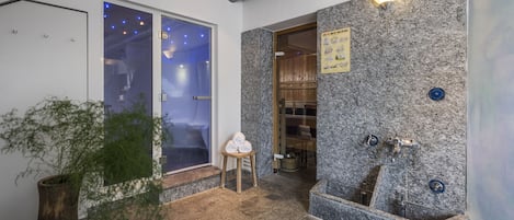 Un área de spa con pared de piedra, puerta de cristal, soporte para toallas y una planta en maceta.