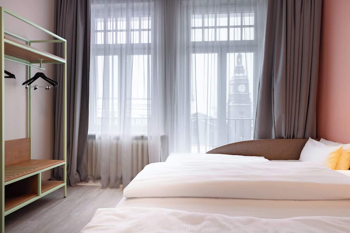 Ein Hotelzimmer mit einem Bett, einem grünen Metallschrank und einem Fenster mit Vorhängen.