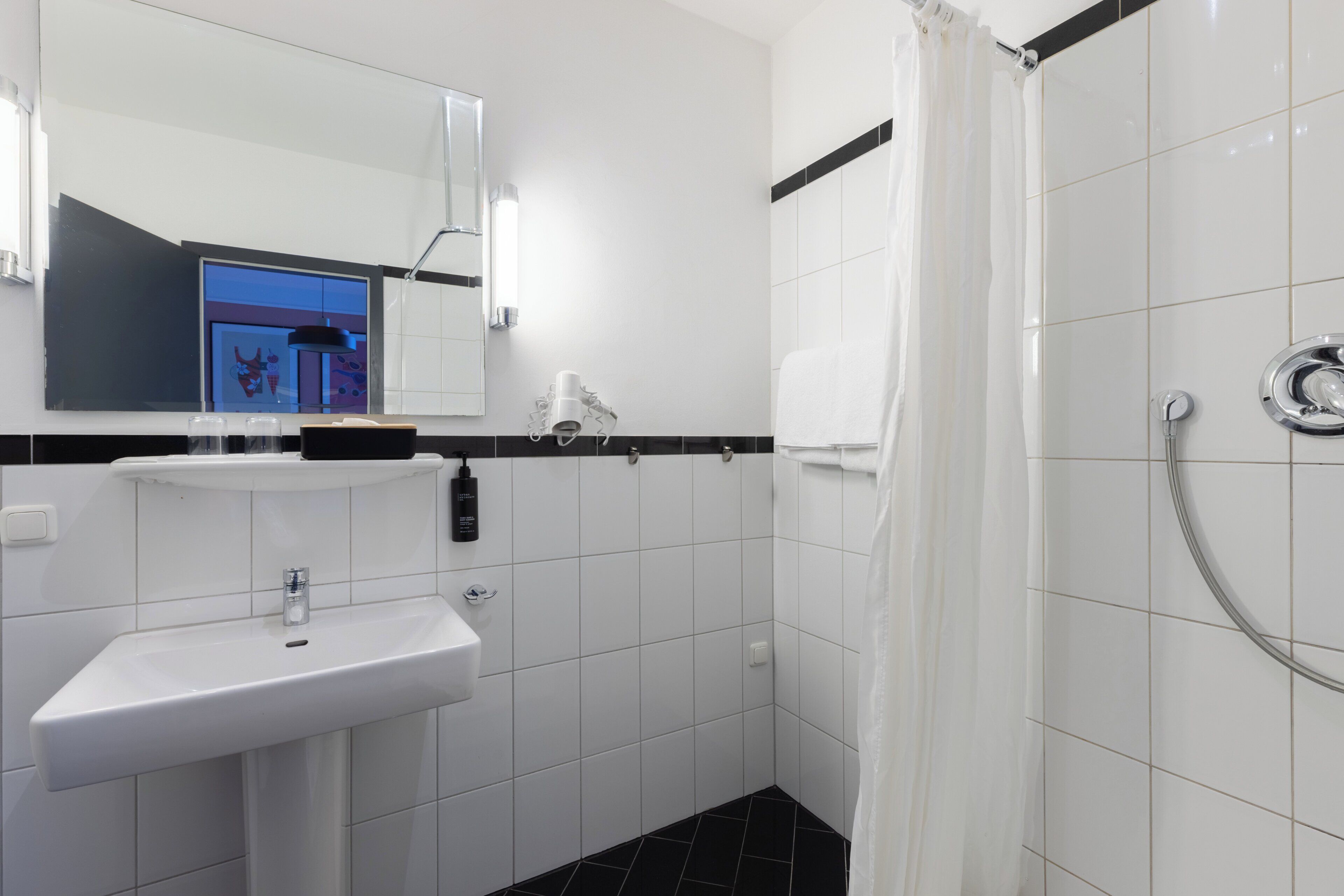 A bathroom with a white sink, a mirror, a shower with a curtain, and a towel rack.