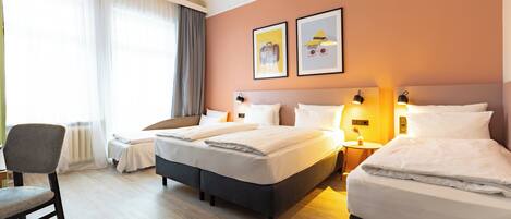 Hotellihuone, jossa on kaksi sänkyä, tuoli, pöytä ja taideteos seinällä.