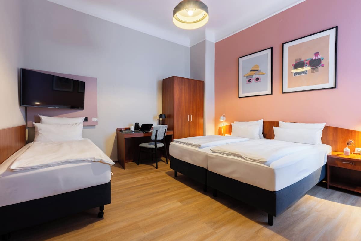 Ein Hotelzimmer mit zwei Betten, einem Schreibtisch, einem Fernseher und Bildern an den Wänden.
