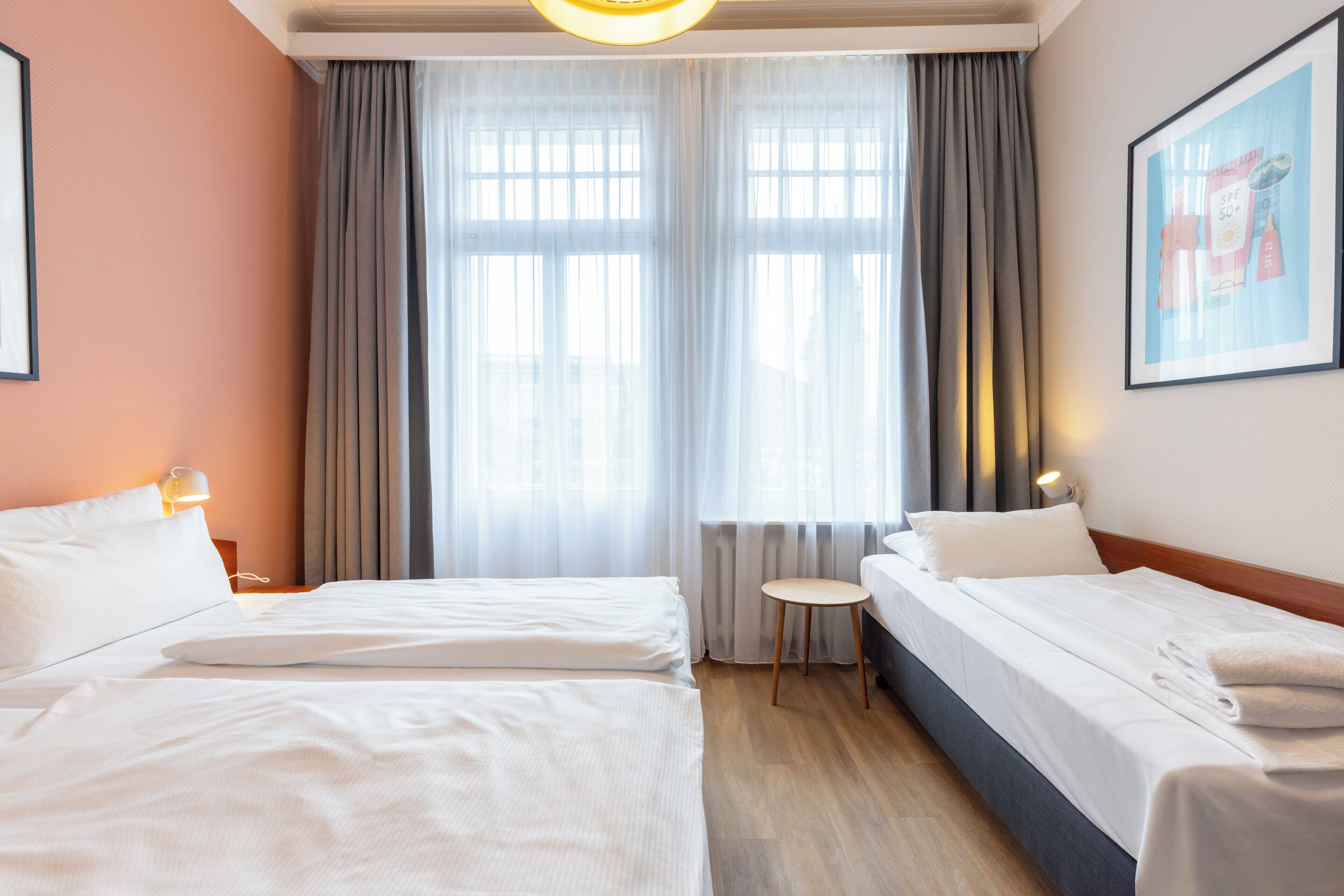 A hotel room with two beds, a small round table, and a large window with curtains.