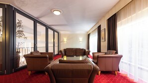 A hotel room with a red carpet, a sofa set, a glass coffee table, and a large window with curtains.