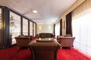 Ein Hotelzimmer mit rotem Teppich, einer Sofagarnitur, einem Glastisch und einem großen Fenster mit Vorhängen.