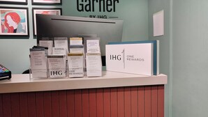 Mostrador de recepción de hotel con obras de arte enmarcadas en la pared, un letrero de IHG ONE REWARDS y varias tarjetas de membresía.