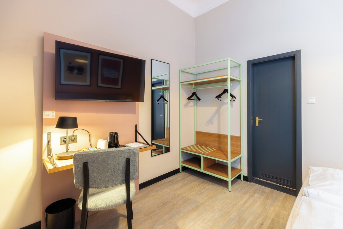 Ein Hotelzimmer mit Schreibtisch, Stuhl, Bett, Kleiderschrank und einer Tür.