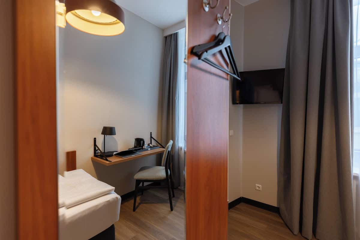 Ein Hotelzimmer mit Bett, Schreibtisch mit Stuhl, Fernseher und einem Fenster mit Vorhängen.