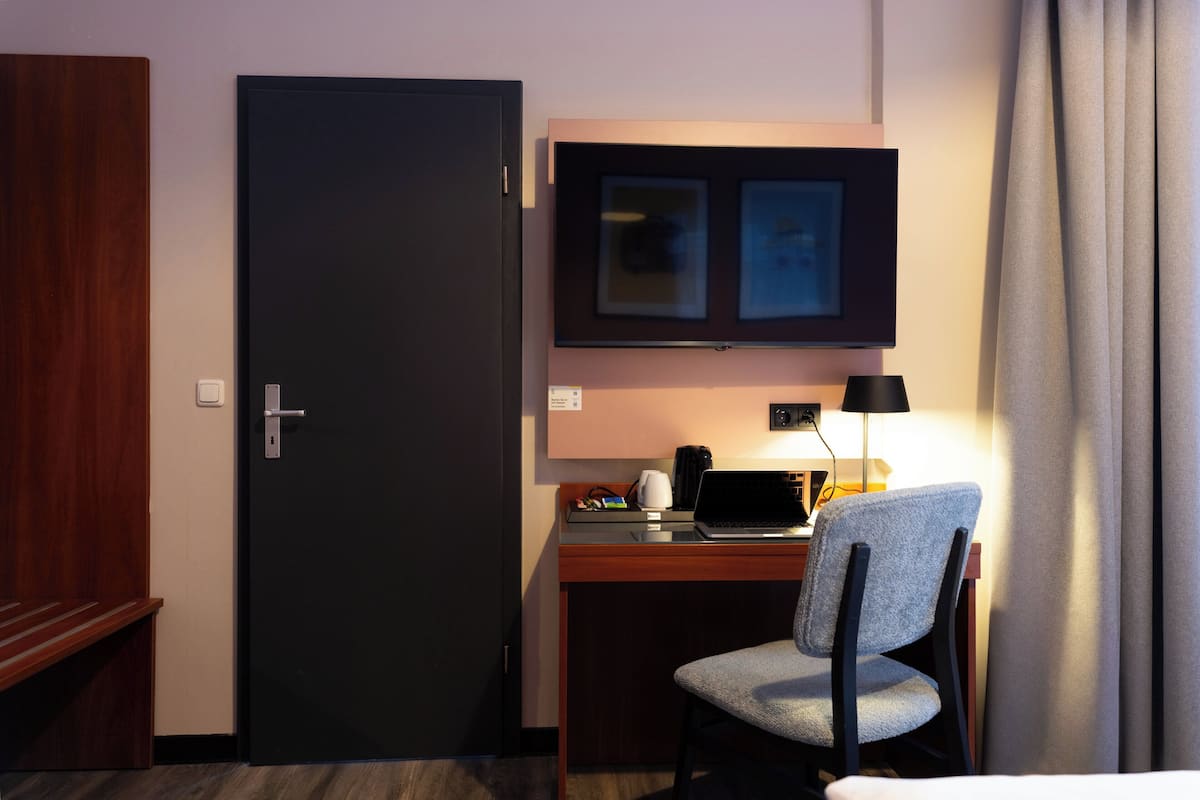 Ein Hotelzimmer mit Schreibtisch, Stuhl, Laptop und einem an der Wand befestigten Fernseher.