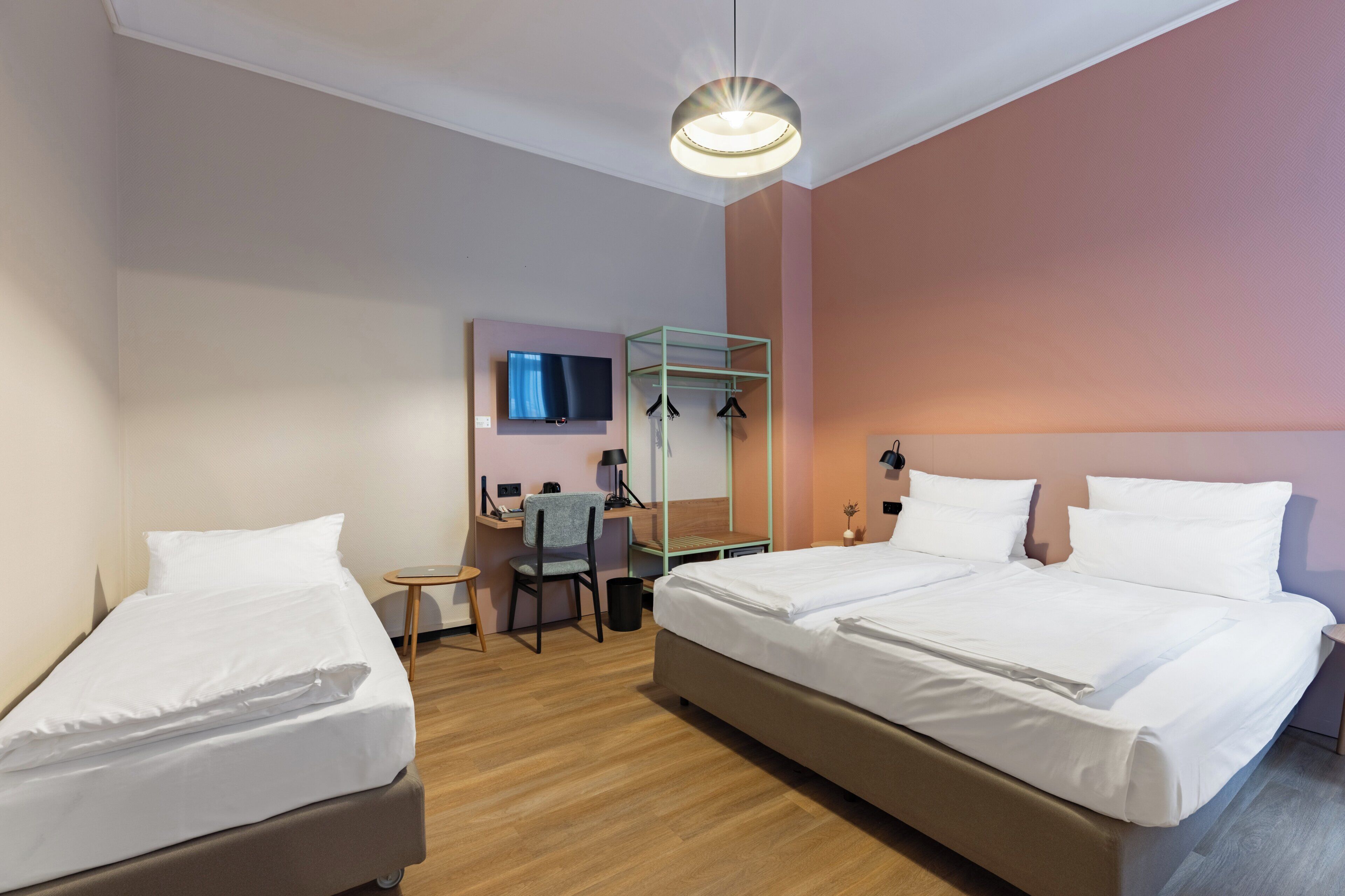 Habitación de hotel con dos camas, un escritorio, una silla, un televisor y una lámpara colgante.
