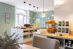 A breakfast bar with a variety of food items, a coffee station, and a seating area with a view of the outdoors. - Garner Hotel Hamburg - St.Georg by IHG (Hamburg)