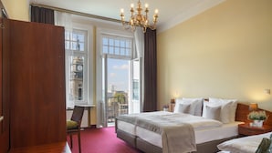 Habitación de hotel con una cama grande, un escritorio, una silla, una mesita de noche y vistas a un paisaje urbano a través de un ventanal amplio.