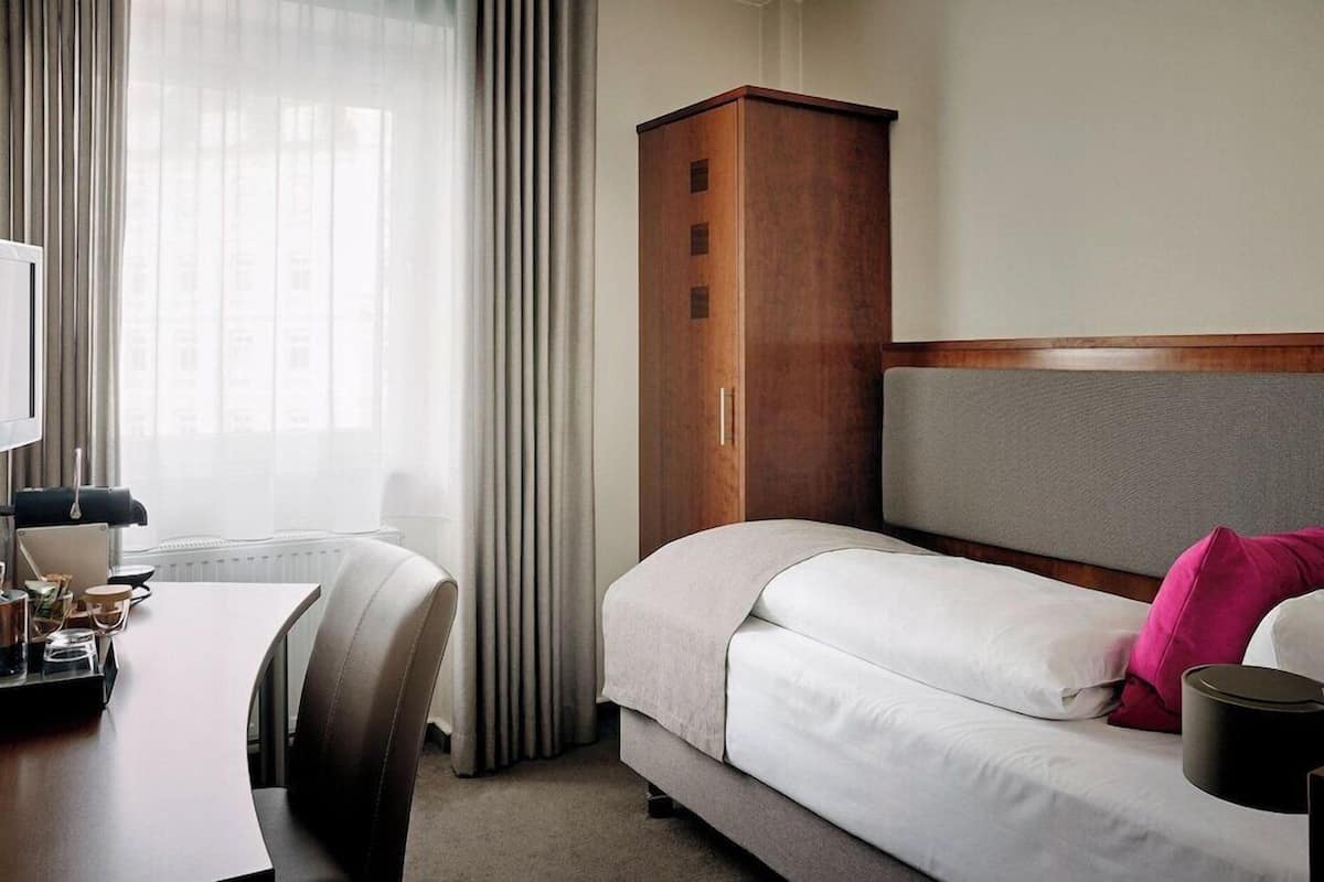Habitación de hotel con cama, armario de madera, escritorio con lámpara y ventana con cortinas.