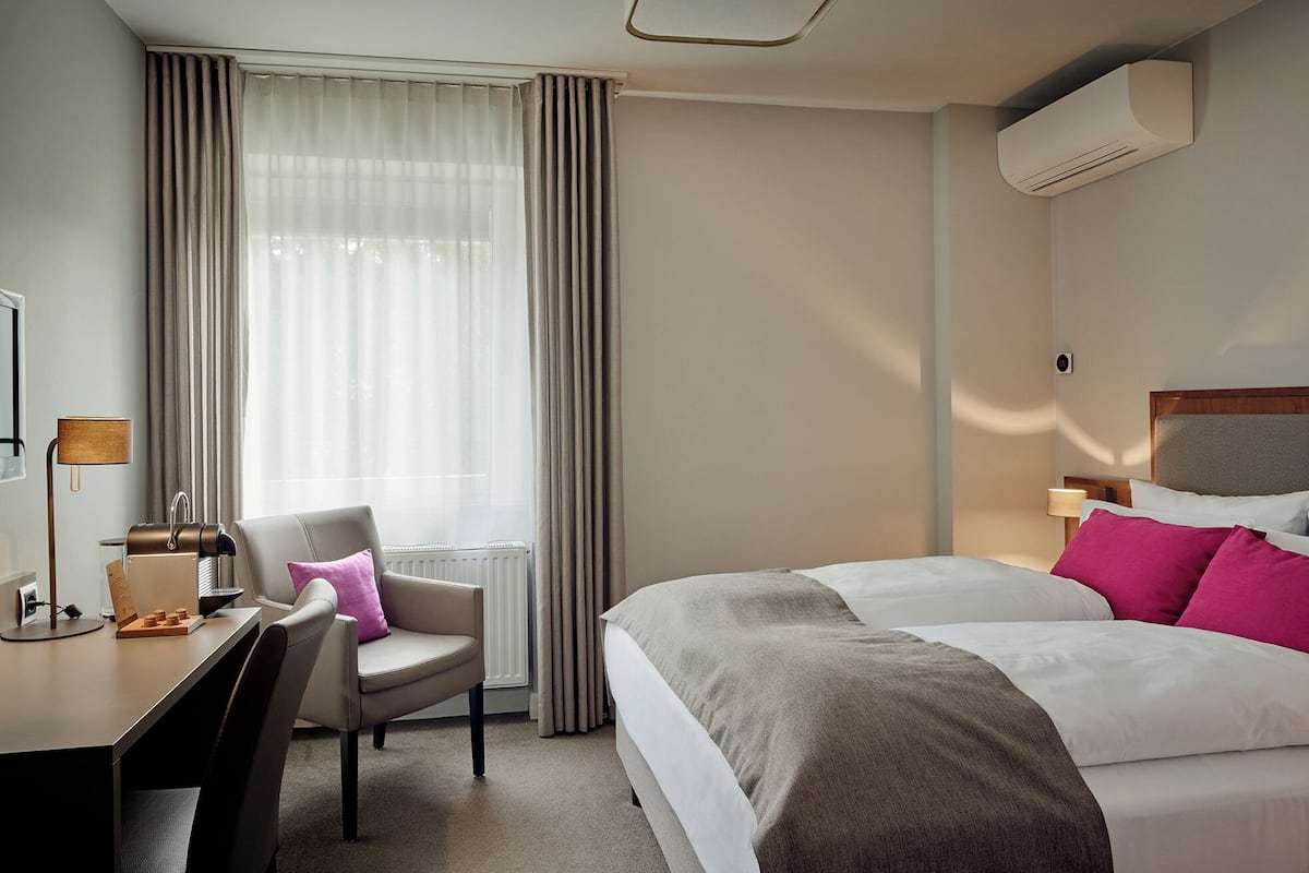 Una habitación de hotel con cama, escritorio, silla y aire acondicionado.