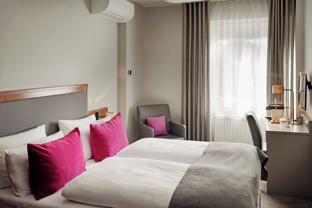 Una habitación de hotel con una cama, un escritorio, una silla y una ventana con cortinas.