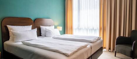 A hotel room with two beds, a chair, and a window with curtains.