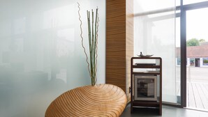 A modern interior with a wooden sculptural bench, a glass wall, and a small wooden cabinet with a decorative item.