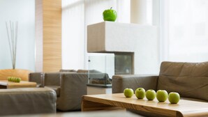 A modern living room with a wooden coffee table, a sofa, and a decorative apple on a shelf.