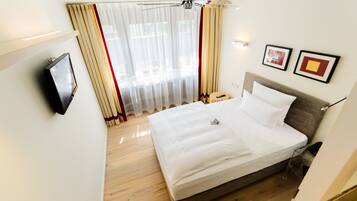 Ein Hotelzimmer mit Bett, Vorhängen, Deckenventilator, Fernseher und zwei gerahmten Bildern an der Wand.