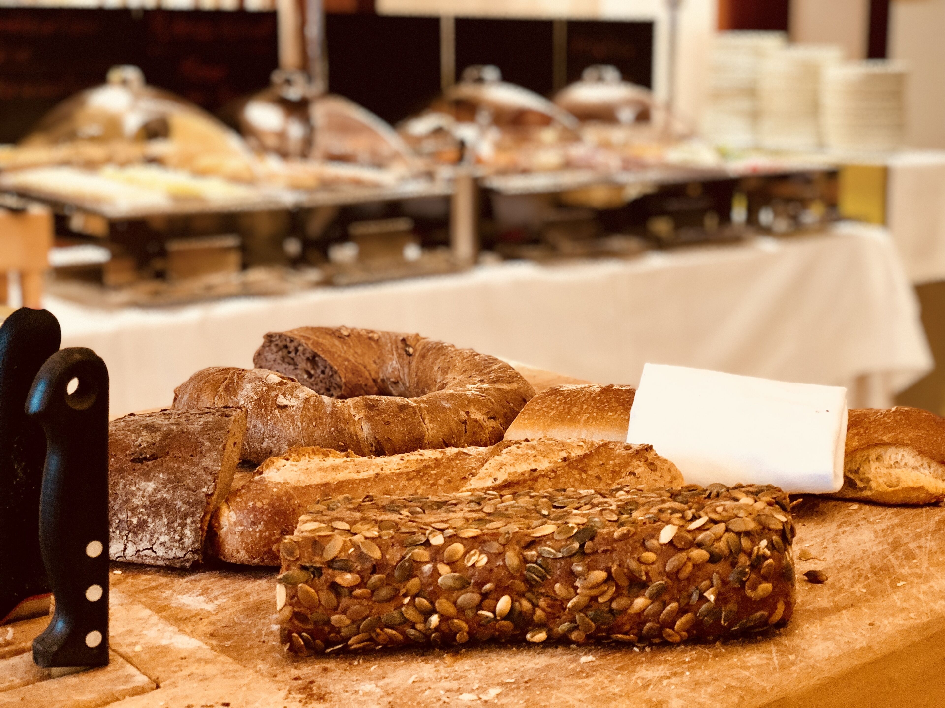 A buffet table with various types of bread, including a loaf with seeds.
