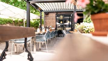 Un patio al aire libre con mesas y sillas, una pérgola y plantas en macetas.