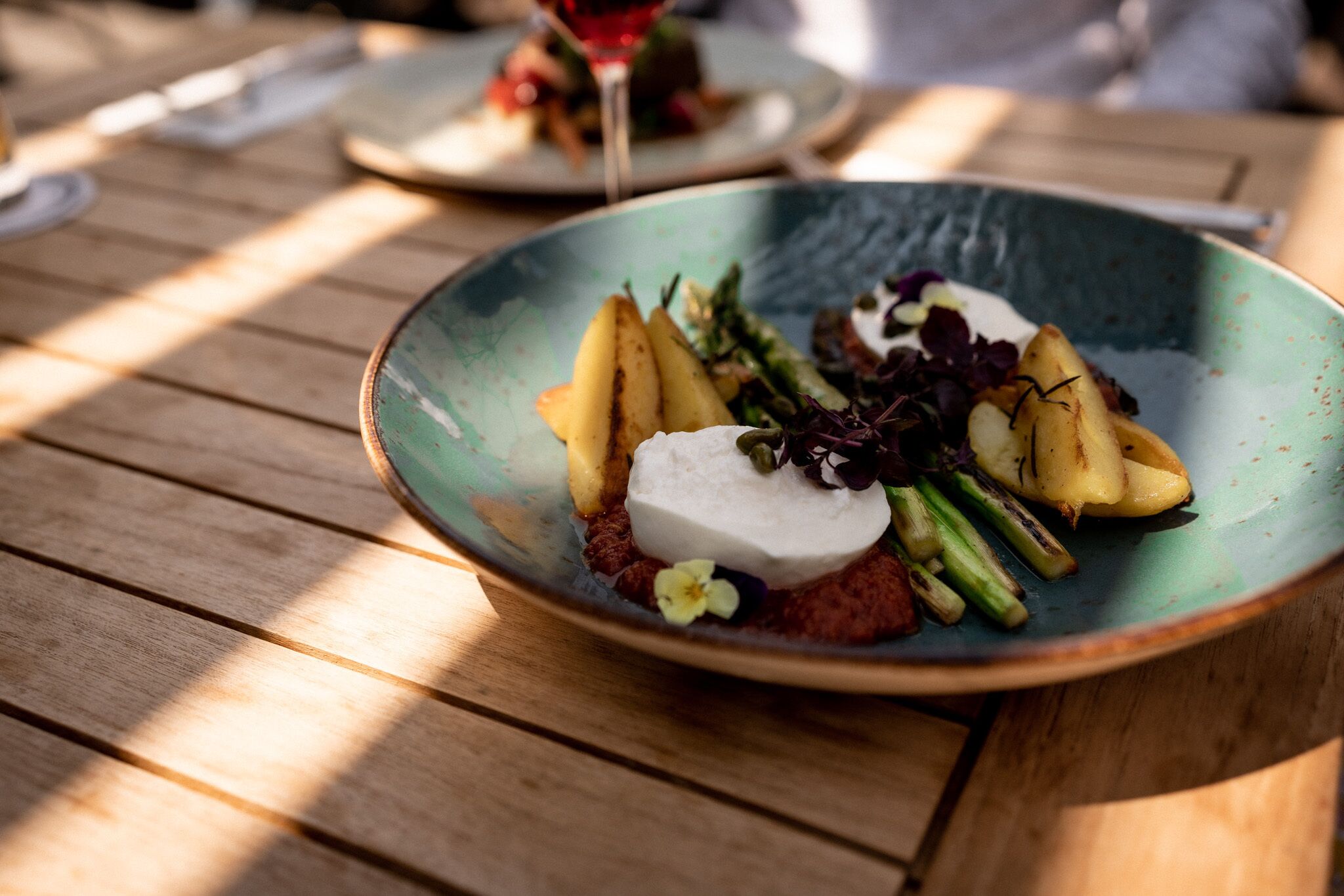 Un plato de comida con patatas, verduras y una cucharada de crema sobre una mesa de madera.
