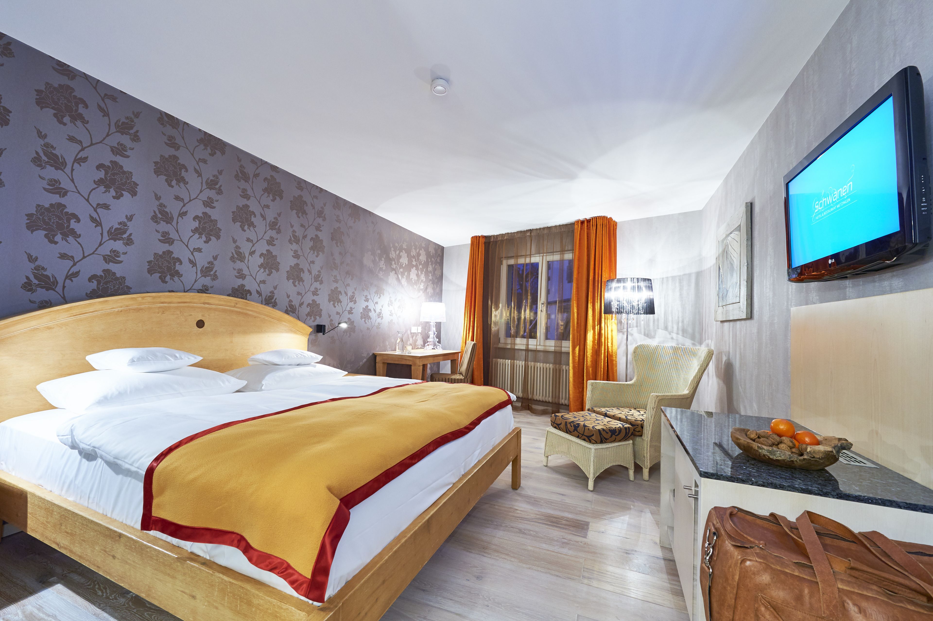 A hotel room with a large bed, a desk with a chair, a television, and a window with curtains.