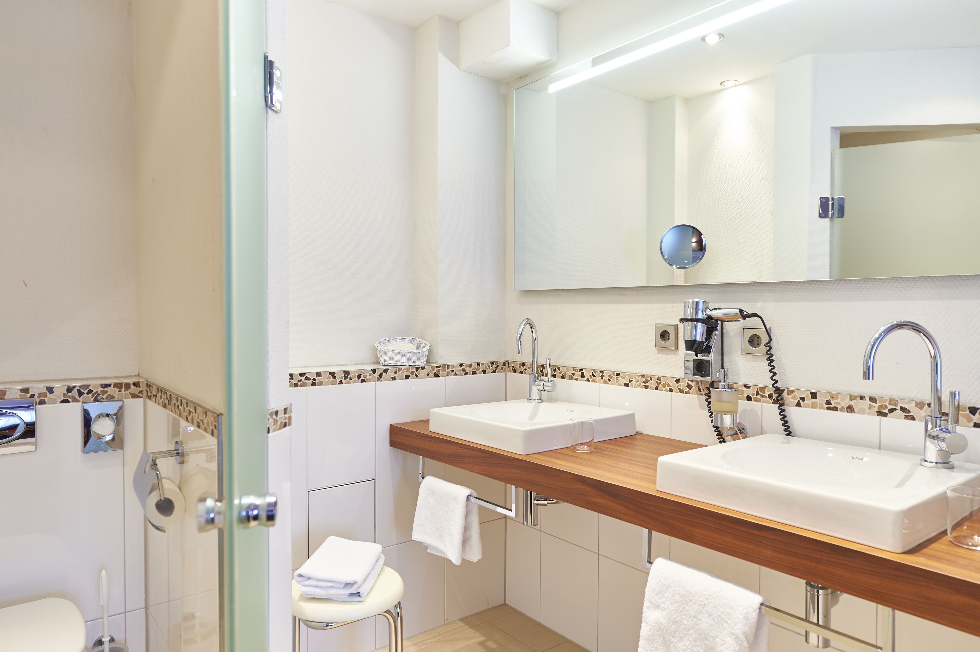 A modern bathroom with two sinks, a glass shower enclosure, and a wooden vanity.
