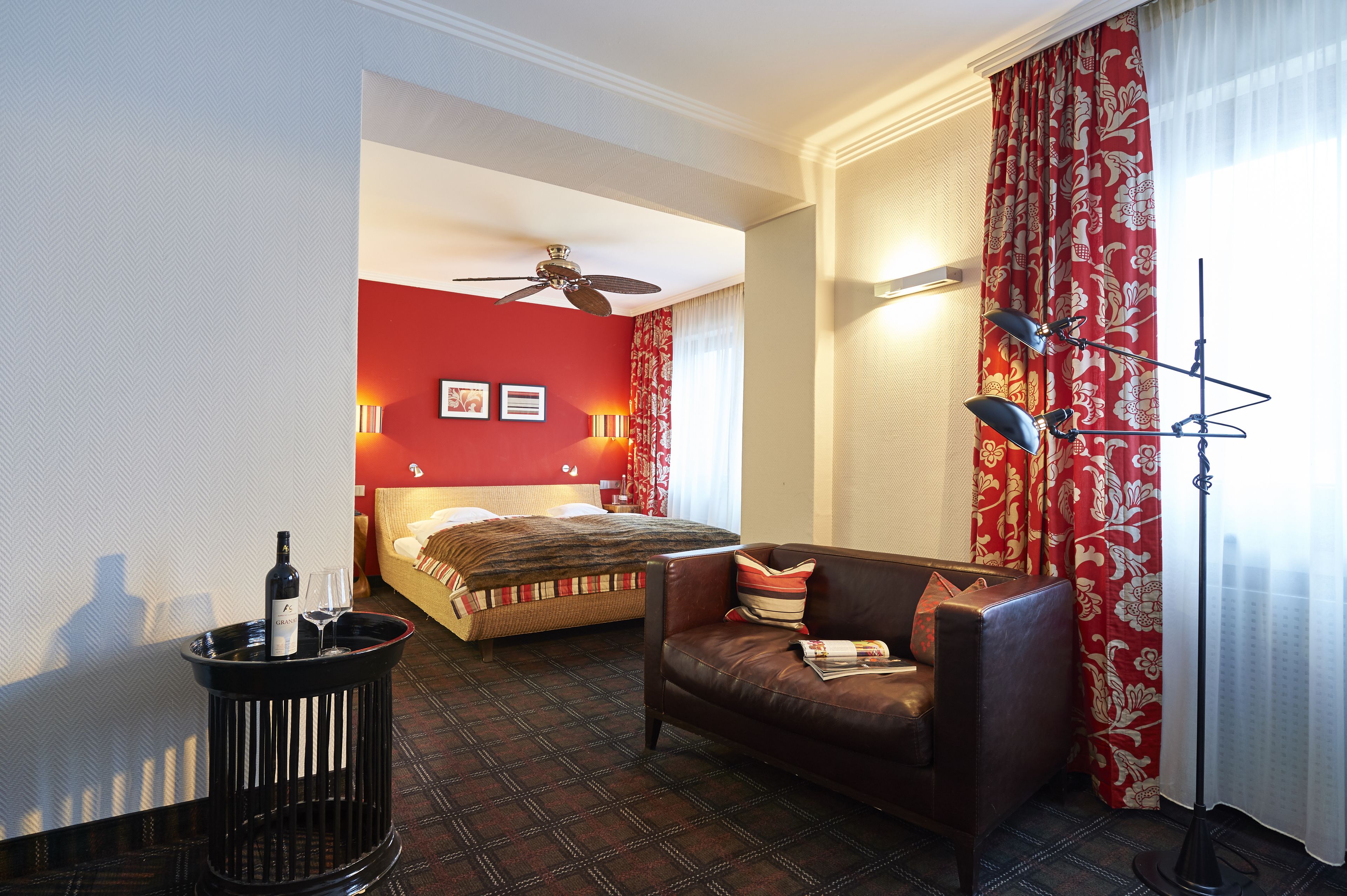 Una habitación de hotel con una cama, un sofá de cuero, una lámpara de pie y una lámpara de suelo.
