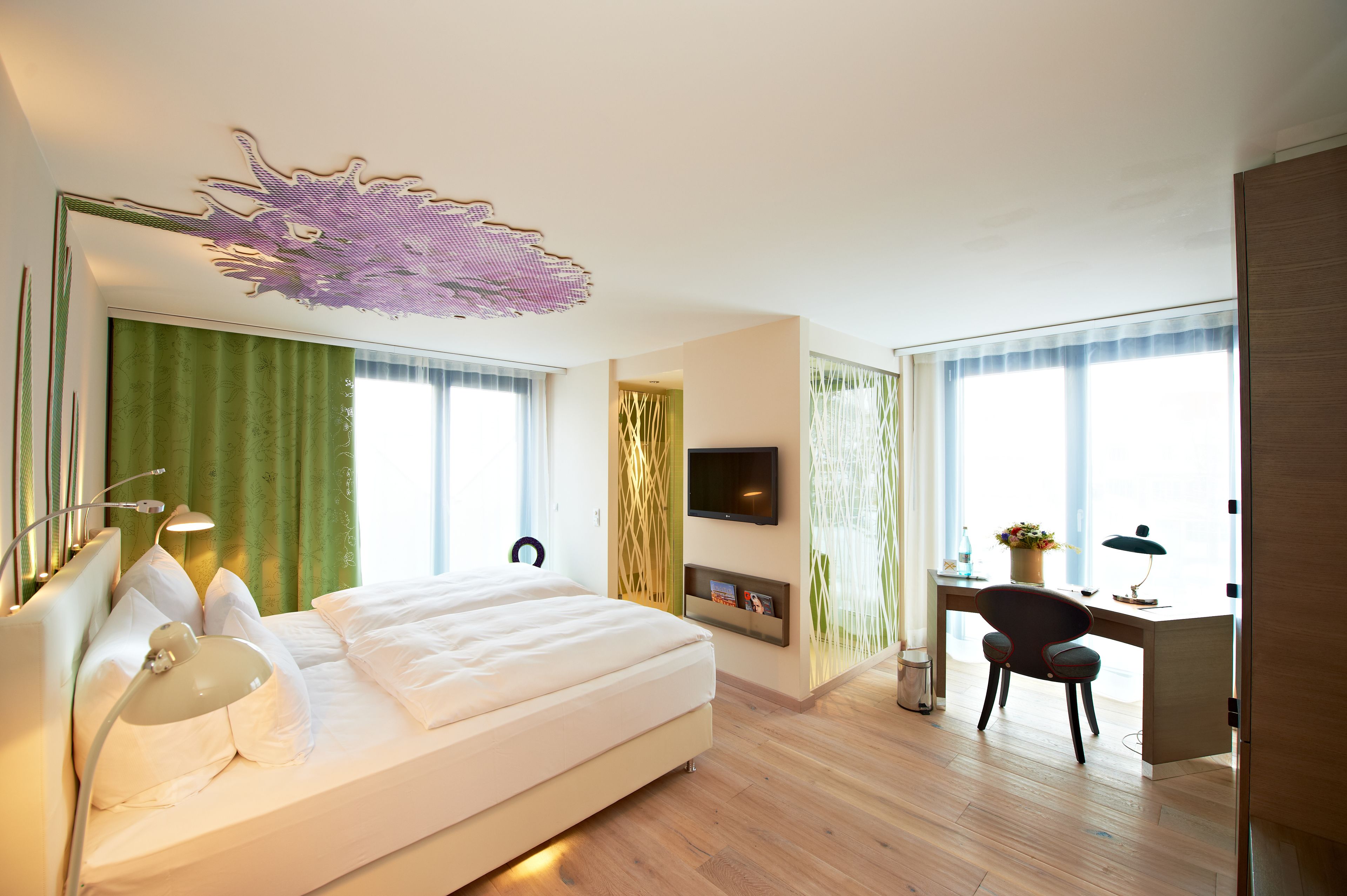 A modern hotel room with a large bed, a desk, and a TV.