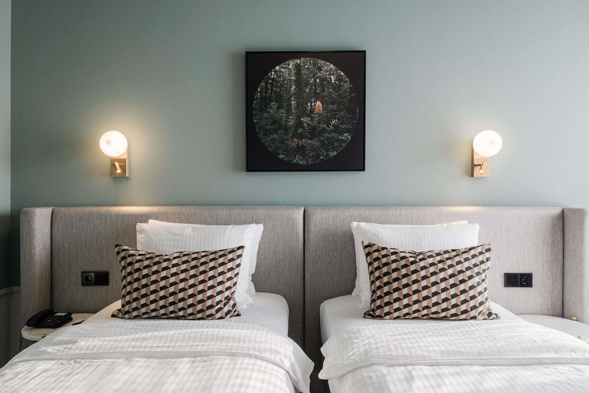 Una habitación de hotel con dos camas, un cuadro en la pared y lámparas de noche.