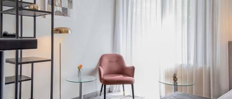 Een moderne woonkamer met een roze fauteuil, een glazen salontafel, een vloerlamp en een boekenkast.
