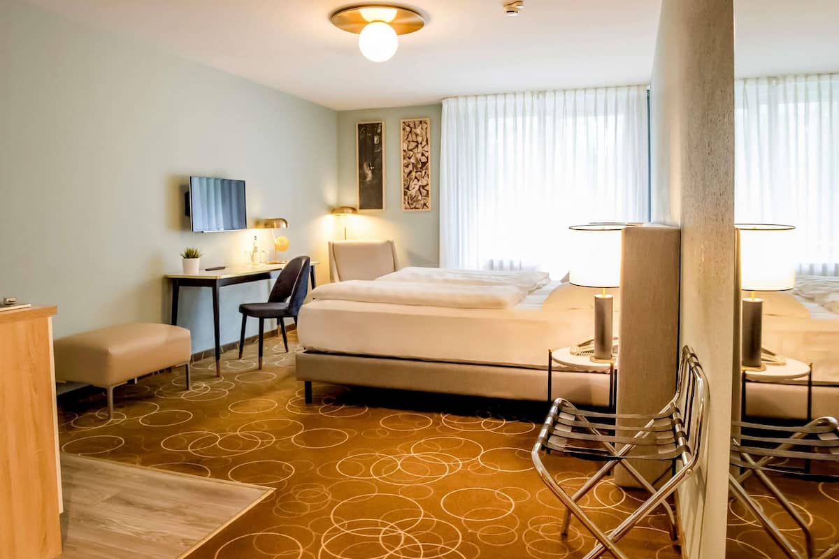 Habitación de hotel con cama, escritorio, silla y vistas al exterior.