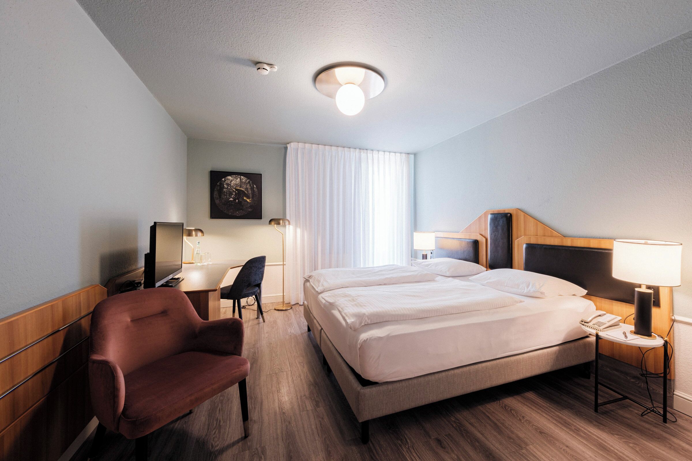 A hotel room with a bed, a desk, a chair, and a lamp.