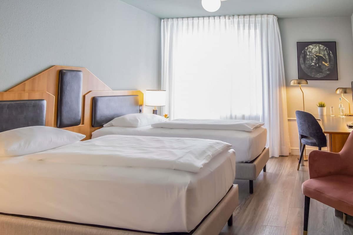 Habitación de hotel con dos camas, un escritorio, una silla y un cuadro en la pared.
