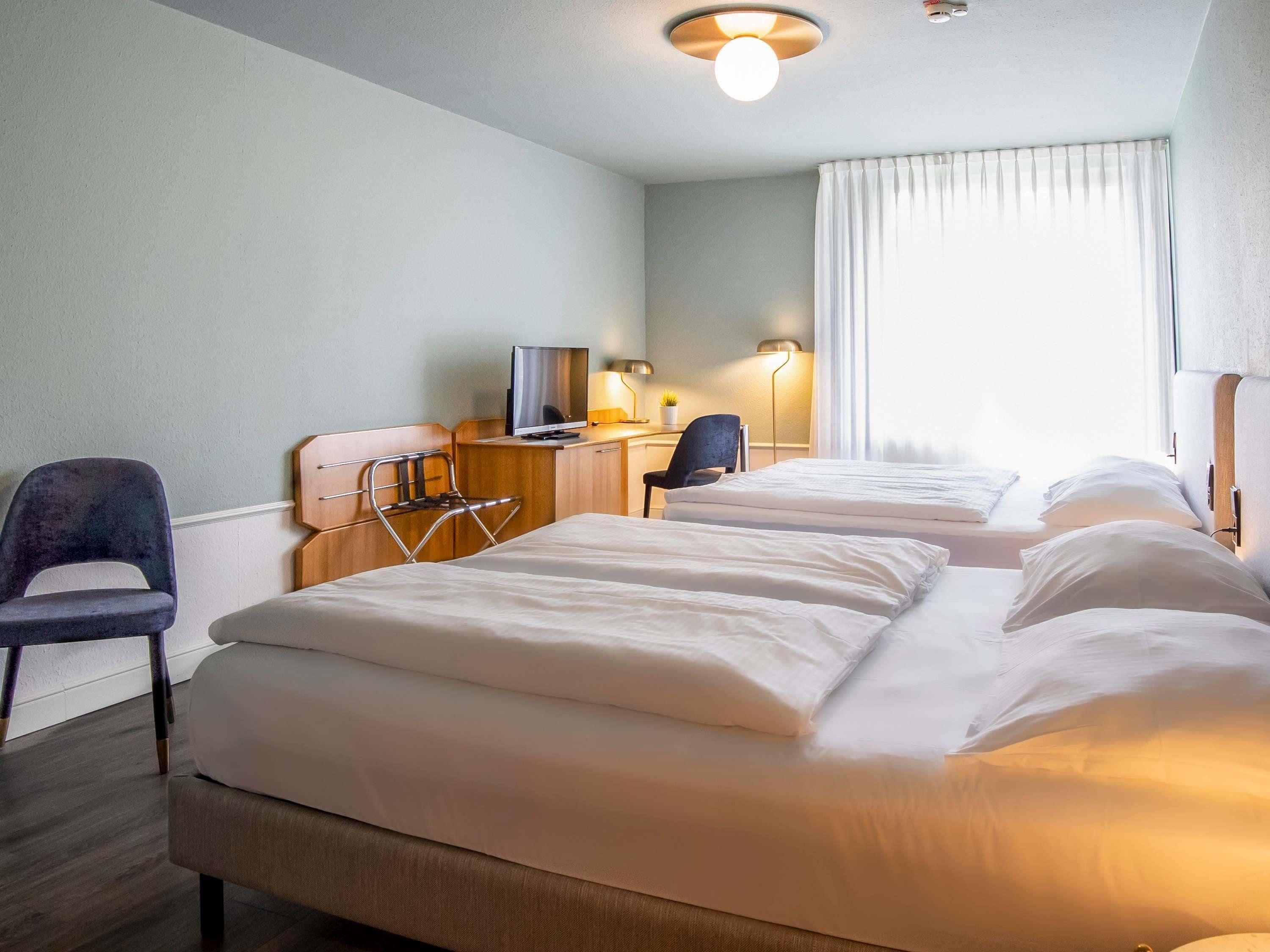 Une chambre d’hôtel avec deux lits, un bureau avec une télévision, une chaise et une lampe.