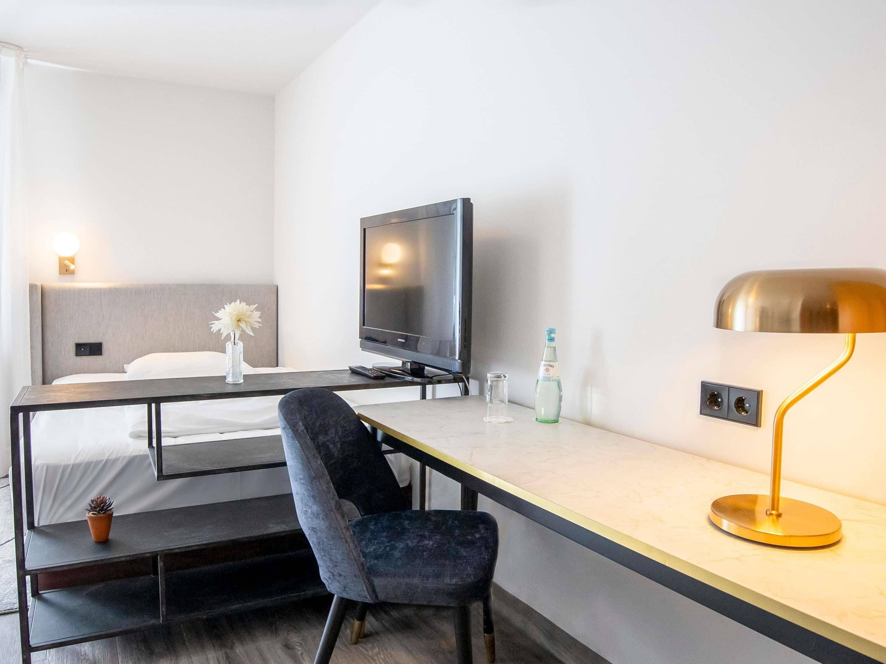 Ein Hotelzimmer mit Bett, Schreibtisch mit Stuhl, Fernseher, Lampe und einer Wasserflasche.