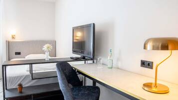 Ein Hotelzimmer mit Bett, Schreibtisch mit Stuhl, Fernseher, Lampe und einer Wasserflasche.