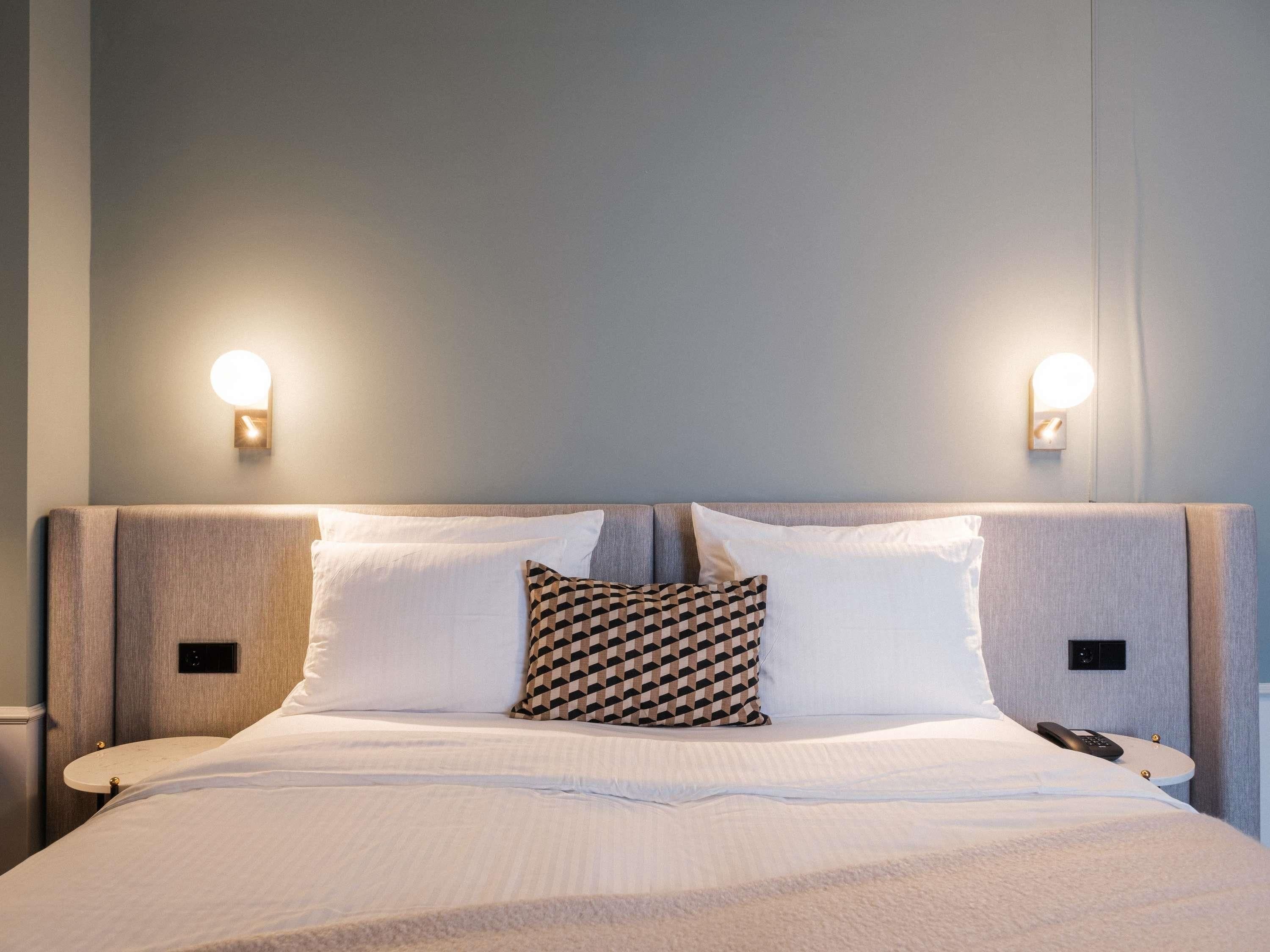 A neatly made bed with white linens, a patterned pillow, and two bedside tables with lamps.